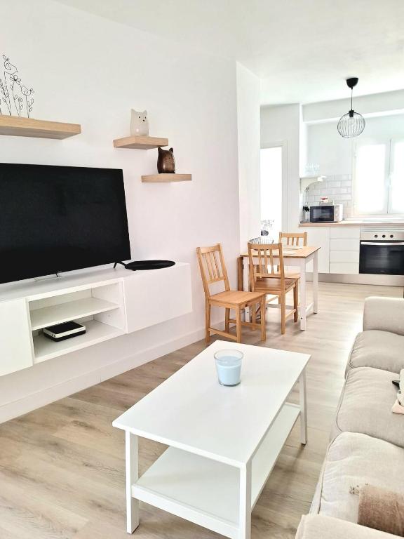 un soggiorno bianco con una grande TV a schermo piatto di La molina, apartamento Cebada a Corralejo