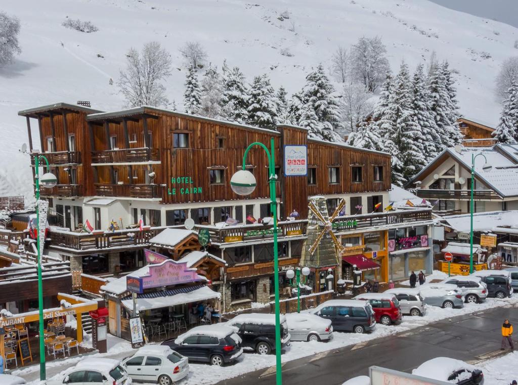 uma cidade coberta de neve com carros estacionados em frente aos edifícios em Hotel Le Cairn em Les Deux Alpes