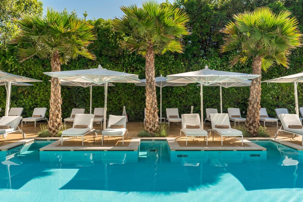 a pool with chairs and umbrellas and palm trees at Resort Miramonti in Forte dei Marmi