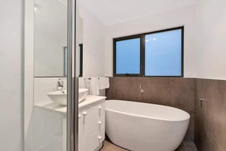 a white bathroom with a tub and a sink at Treetops-Large Home 9km to CBD Sleeps 10 in Hobart