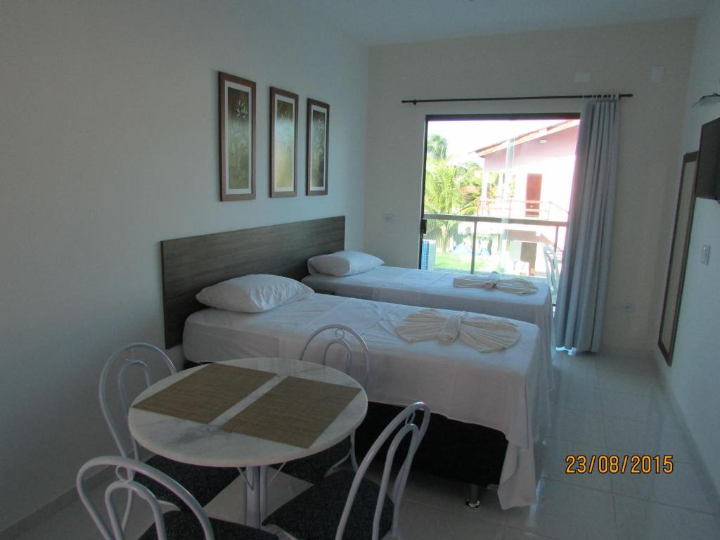 a bedroom with two beds and a table and a window at Pousada Sky Beach Flat in Porto De Galinhas