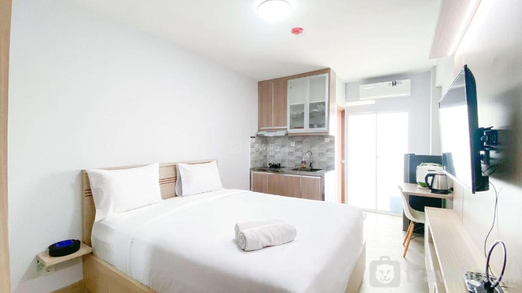 a bedroom with a large white bed and a kitchen at Cozy Living and Homey Studio Room Cinere Resort Apartment By Travelio in Depok