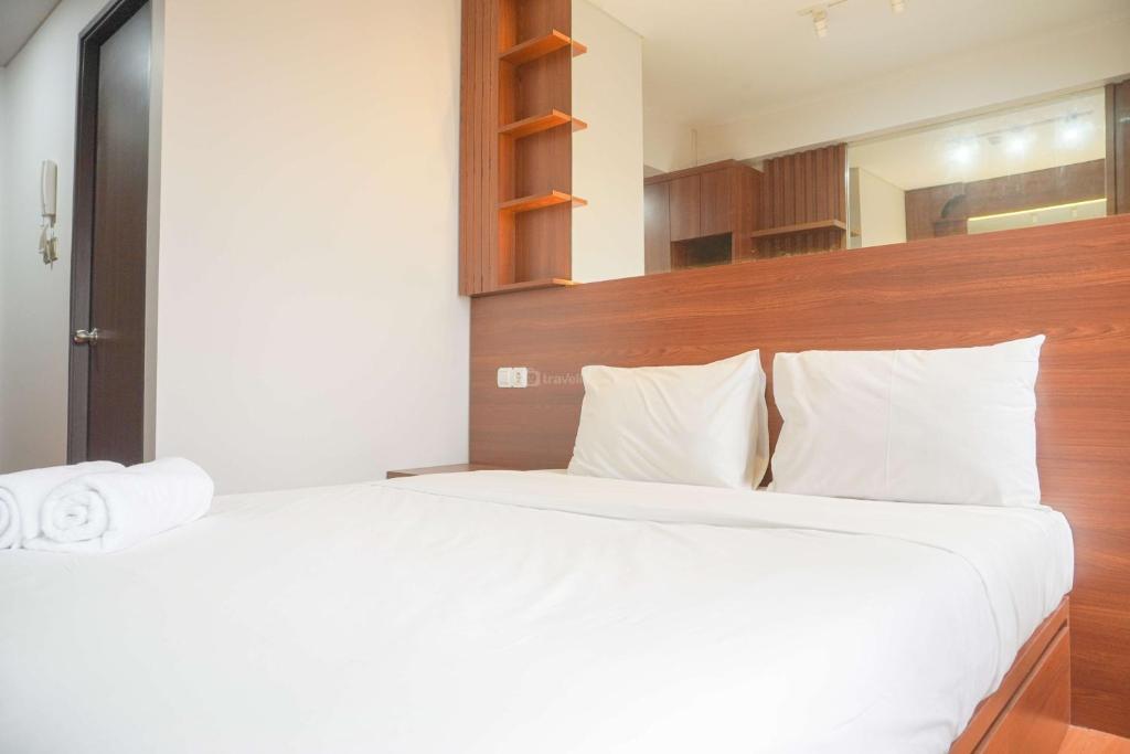 a bedroom with a white bed with a wooden headboard at Relaxing and Homey Studio Transpark Cibubur Apartment By Travelio in Depok