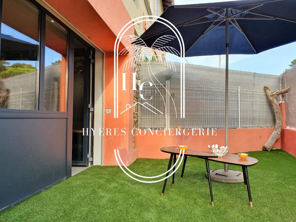 une table avec un parasol devant un bâtiment dans l'établissement Le Bois d'Olivier T2 à Giens CLiM WiFi Parking By HC, à Hyères