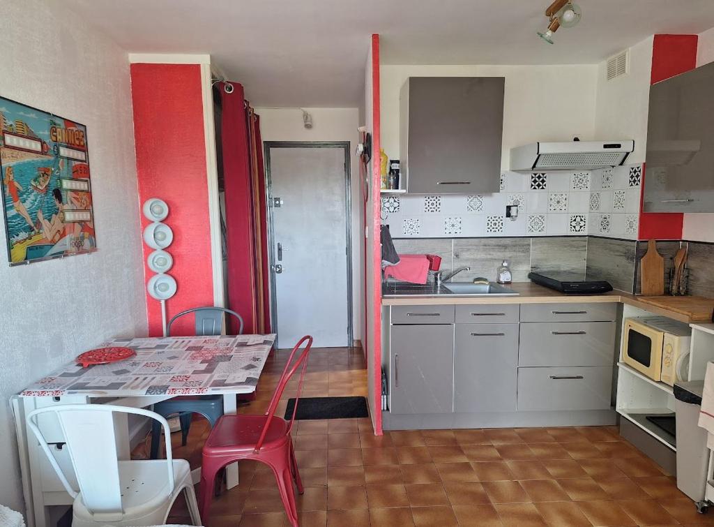 une petite cuisine avec une table et des touches rouges dans l'établissement Studio Asphodèles bord de mer, au Cap d'Agde