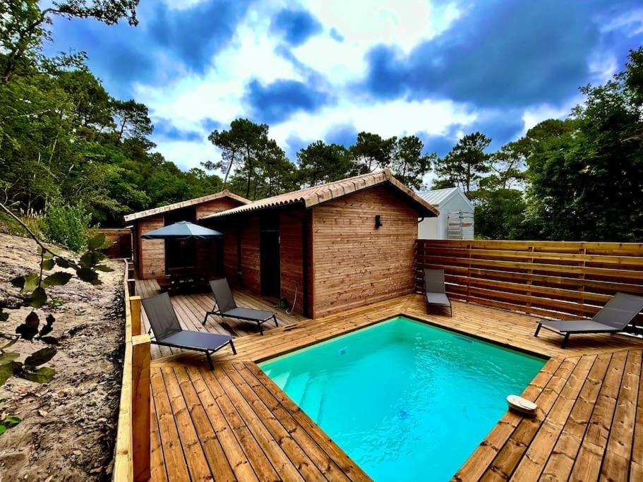 une terrasse en bois avec une piscine et une maison dans l'établissement Villas climatisées avec piscine et SPA proche du lac, à Lacanau
