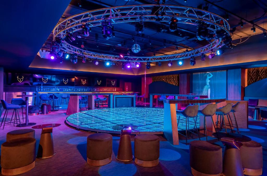 a stage in a room with purple lighting and stools at Desire Riviera Maya Resort All Inclusive - Couples Only in Puerto Morelos