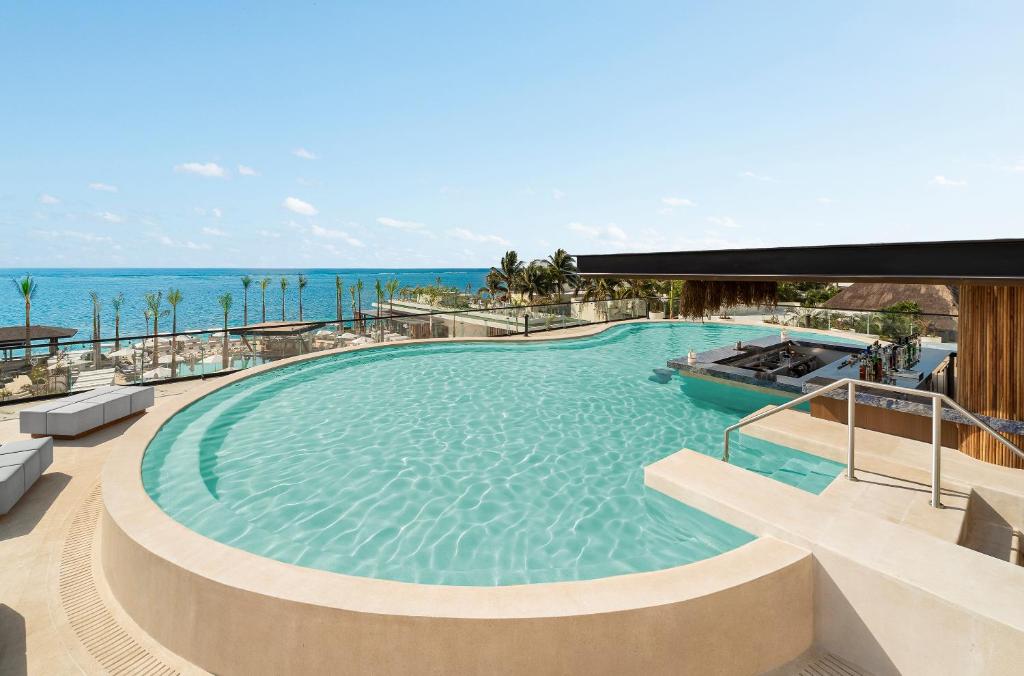 a large swimming pool with the ocean in the background at Desire Riviera Maya Resort All Inclusive - Couples Only in Puerto Morelos