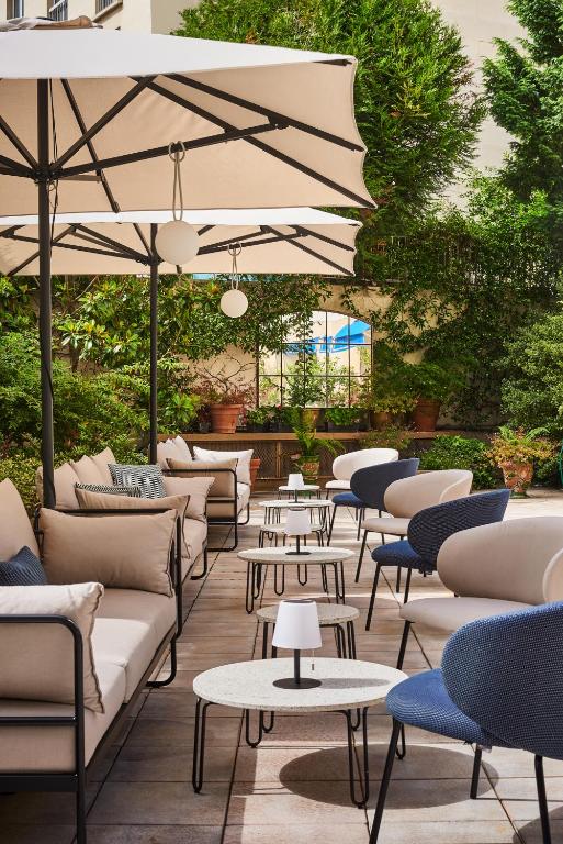 une terrasse avec des canapés, des tables et des parasols dans l'établissement Hôtel Le Versailles, à Versailles