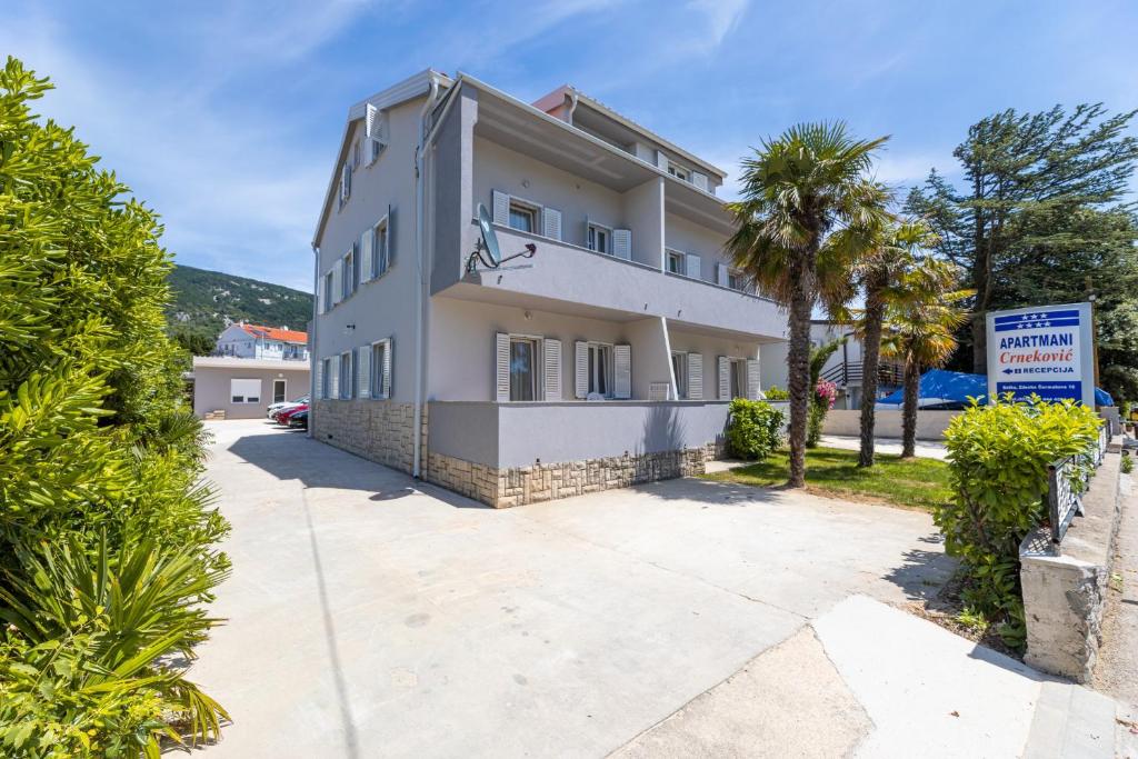 a white building with a palm tree in front of it at Apartments Crnekovic IX in Baška