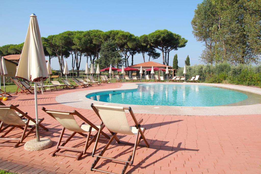 eine Gruppe Stühle und ein Pool mit Sonnenschirm in der Unterkunft La Fattoria di Tirrenia in Tirrenia
