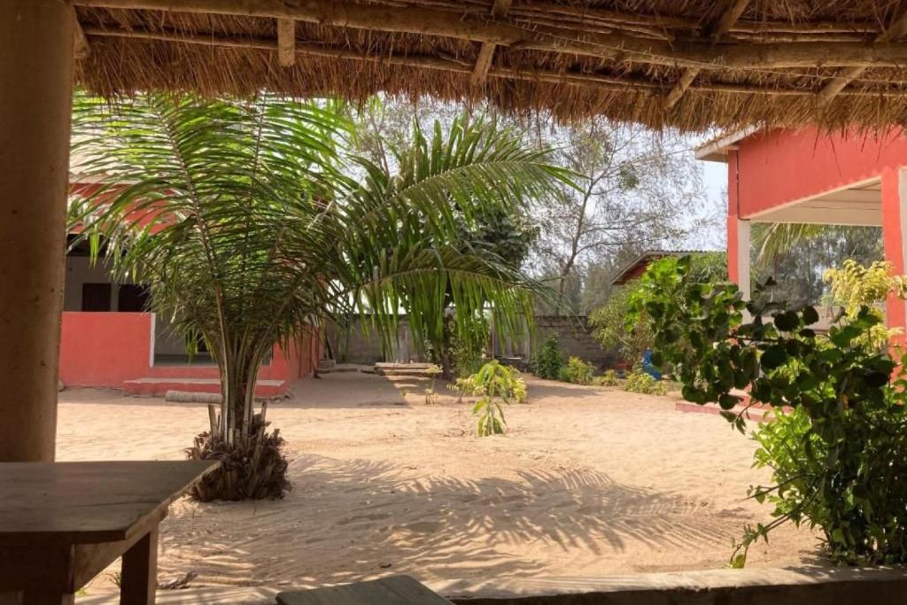 a courtyard with palm trees and a red building at Appart'Haris in Ouidah