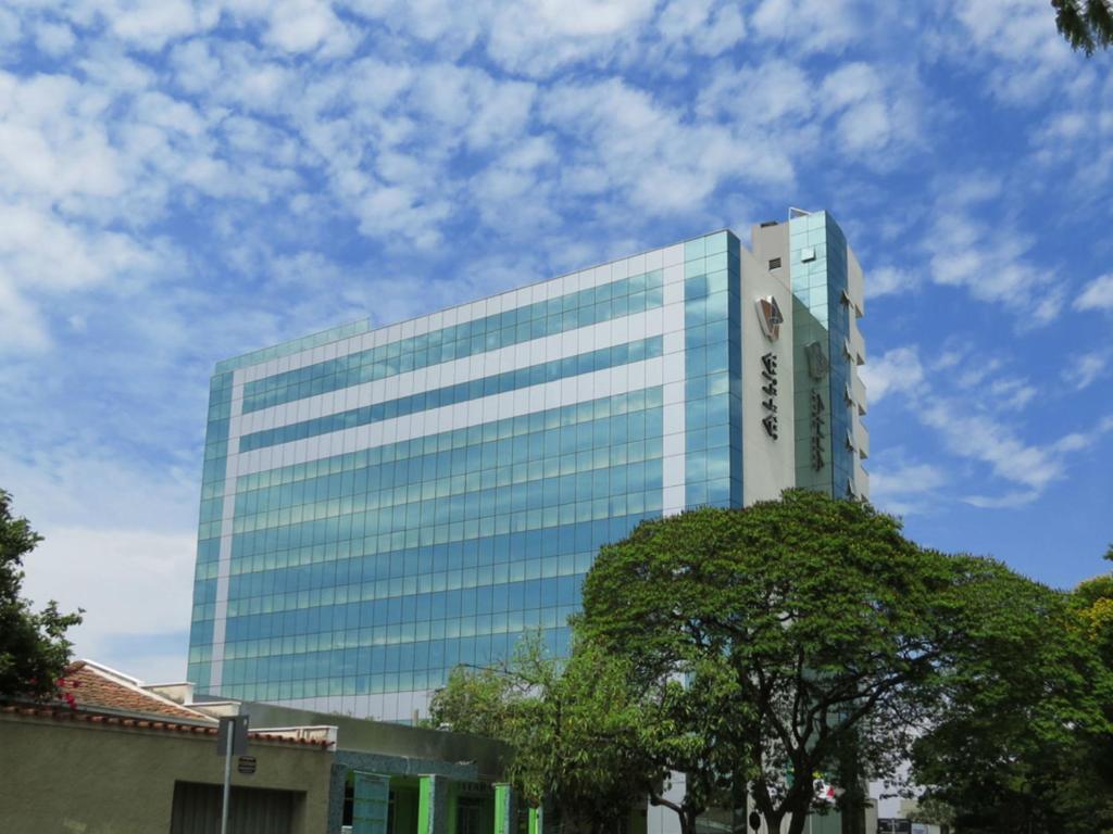 un edificio de cristal alto con un árbol delante de él en Allia Gran Pampulha Suites, en Belo Horizonte