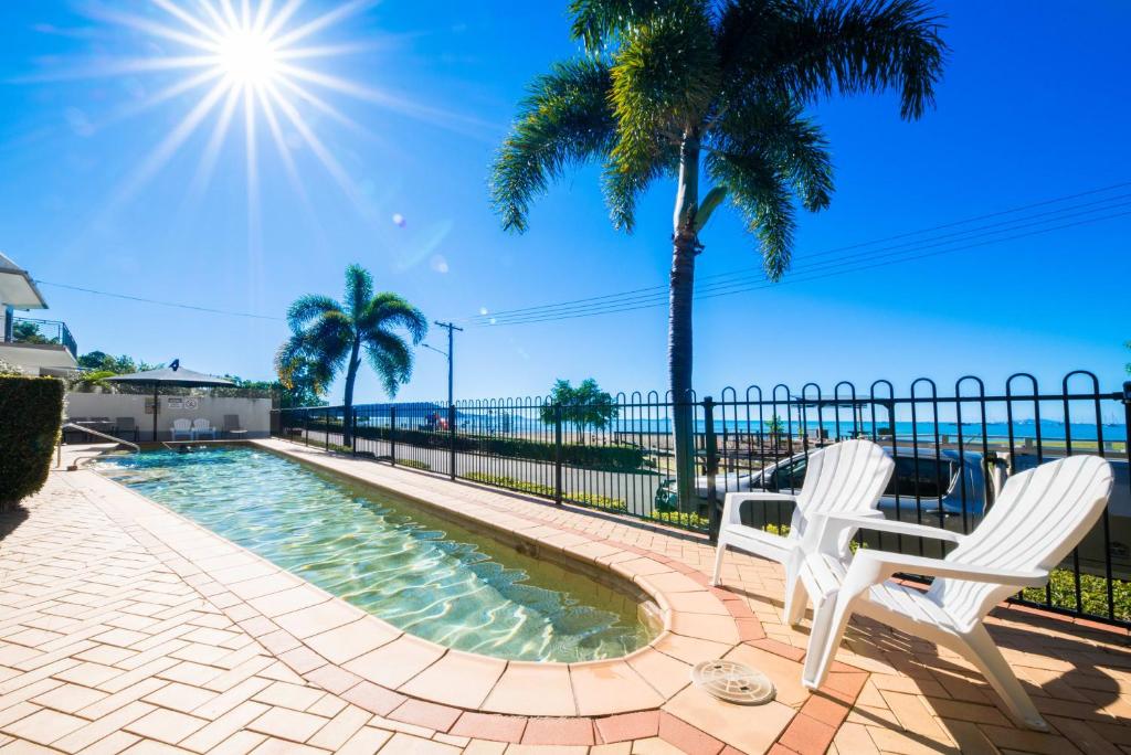 a swimming pool with two white chairs and palm trees at Whitsunday Beachfront Apartment on Coral Esplanade in Cannonvale