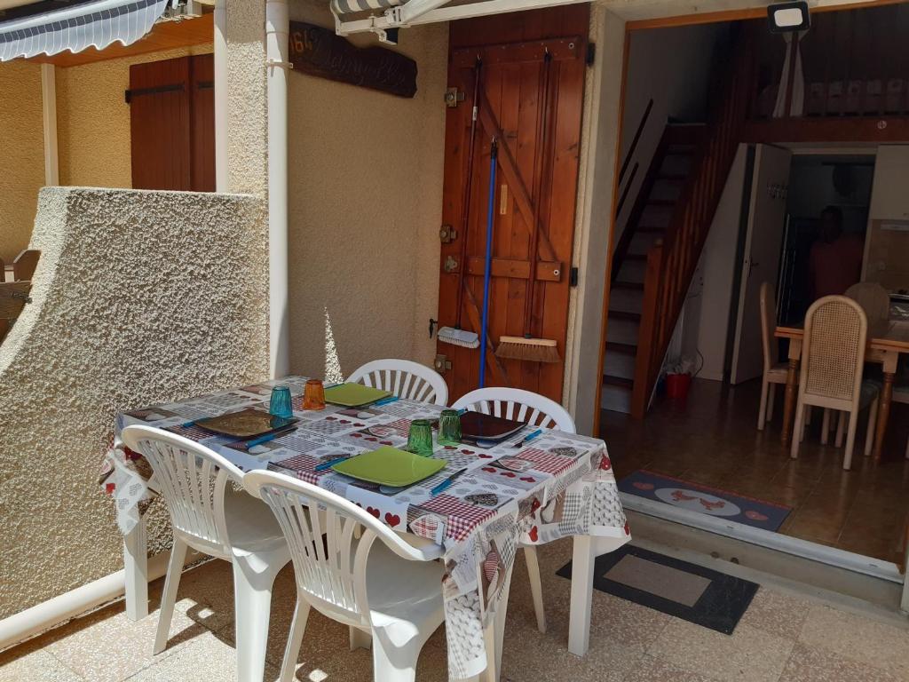 une table avec des chaises blanches et une table avec un tissu de table dans l'établissement Villa Climatisée avec Mezzanine, Parking Sécurisé et Terrasse près du Lac Marin pour 4 Personnes - FR-1-798-42, à Leucate