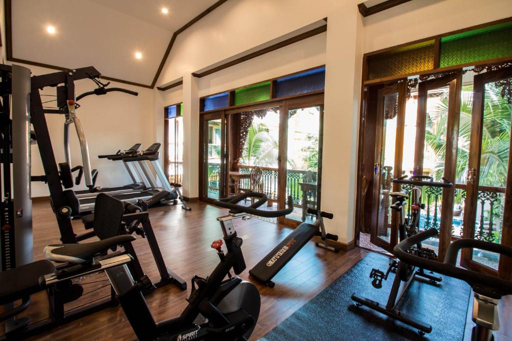 A bright fitness room contains cardio machines, a multi-gym, benches, and free weights beside courtyard windows.