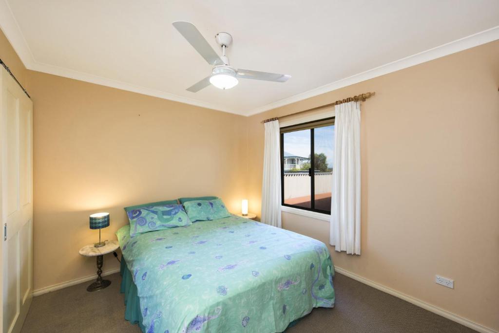 a bedroom with a bed with a ceiling fan and a window at Sea Change - Spacious Family Holiday Accommodation Pet friendly in Ledge Point