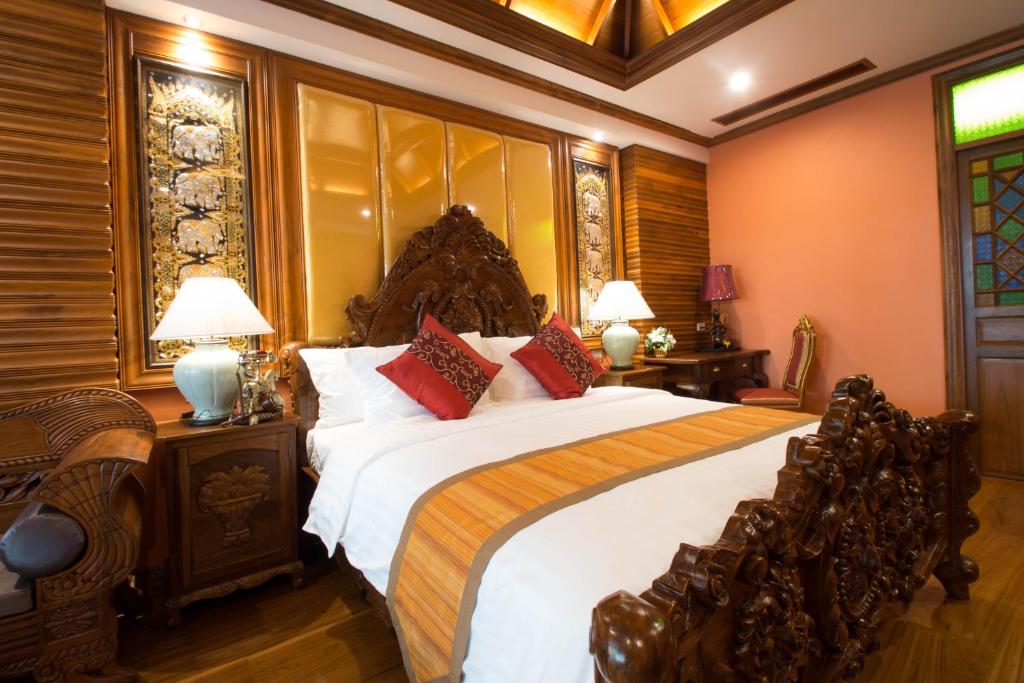 A traditional bedroom with an ornate carved headboard, upholstered wall panels and a richly finished timber ceiling.