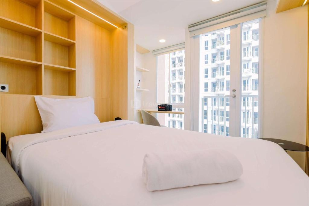 un letto bianco in una stanza con una grande finestra di Simply Look and Cozy Studio Tokyo Riverside PIK 2 Apartment By Travelio a Rawalembang