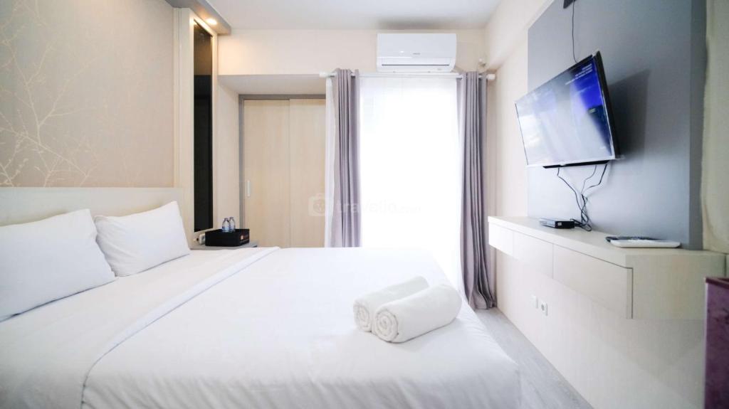 a hotel room with a white bed with a flat screen tv at Best Deal and Restful Studio Apartment Suncity Residence By Travelio in Sidoarjo
