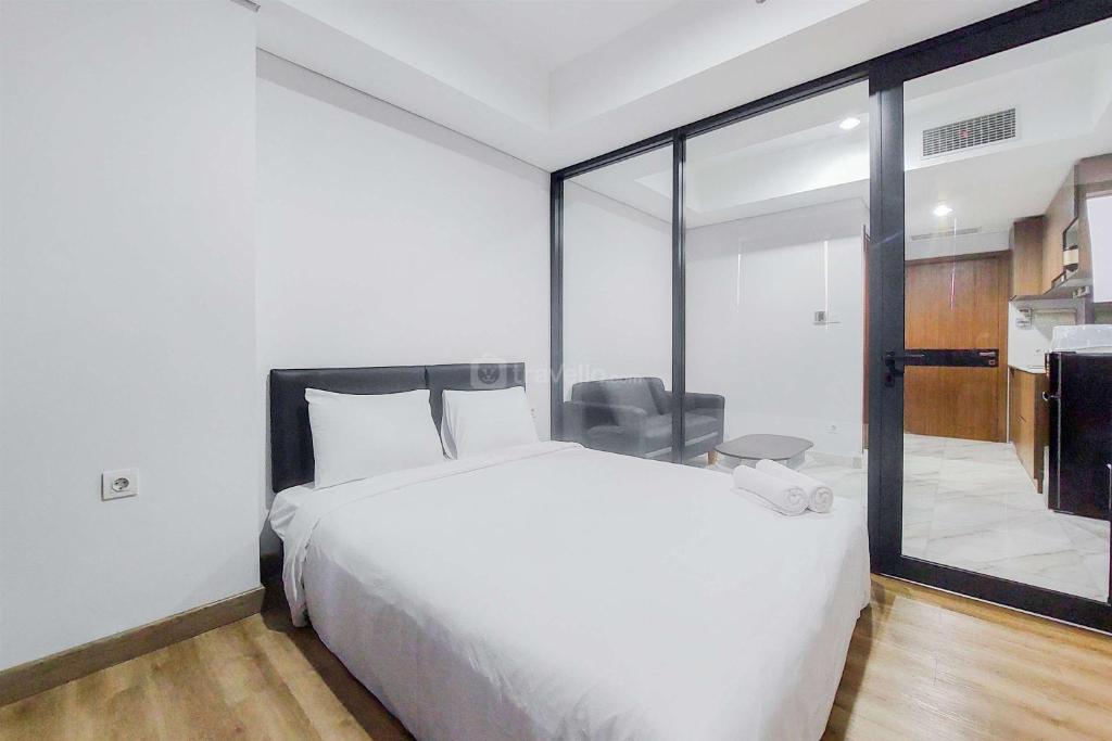 - une chambre avec un lit blanc et une porte coulissante en verre dans l'établissement Tranquil and Comfort Living 1BR The Smith Alam Sutera Apartment By Travelio, à Tangerang