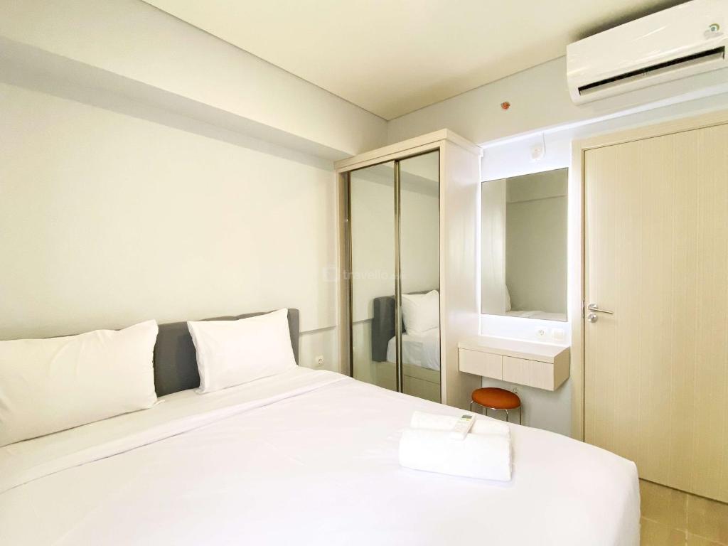a bedroom with a white bed and a mirror at Best Deal and Cozy 3BR Meikarta Apartment By Travelio in Cikarang
