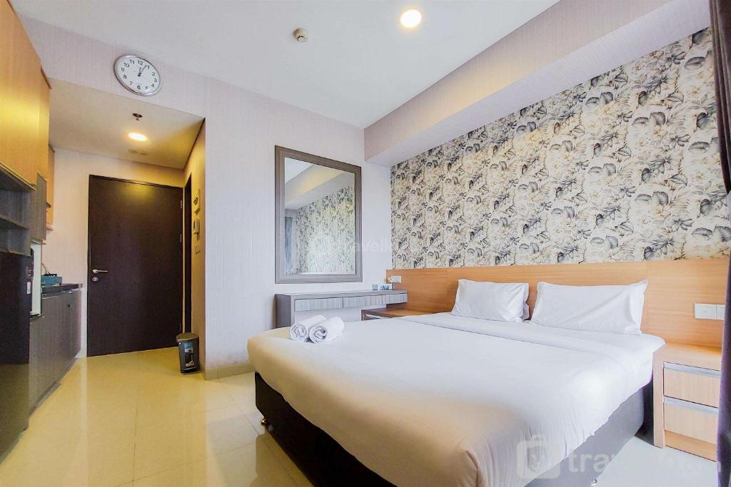 a bedroom with a large white bed and a clock on the wall at Fancy and Nice Studio at Atria Residence Gading Serpong Apartment By Travelio in Tangerang