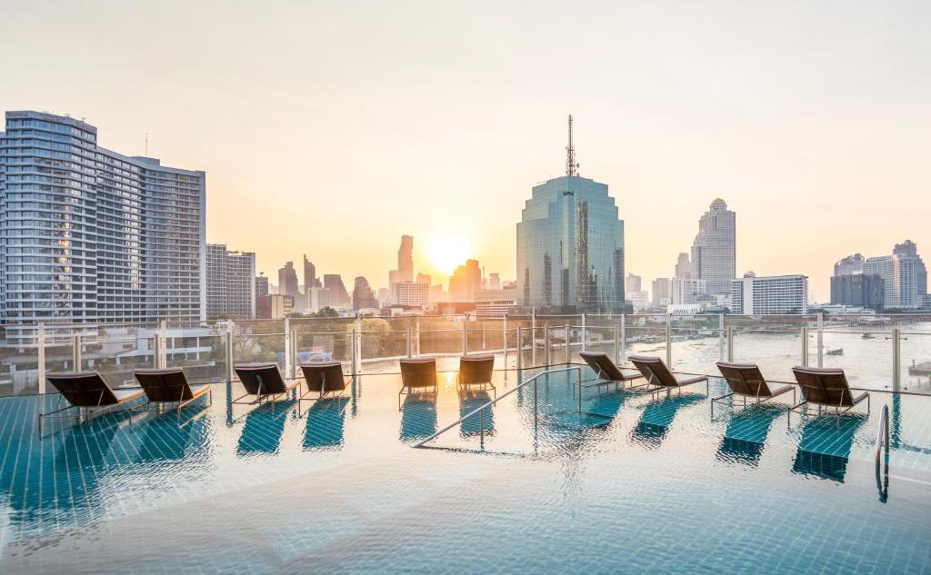 An elevated pool deck overlooks a broad Bangkok skyline and riverfront cityscape.