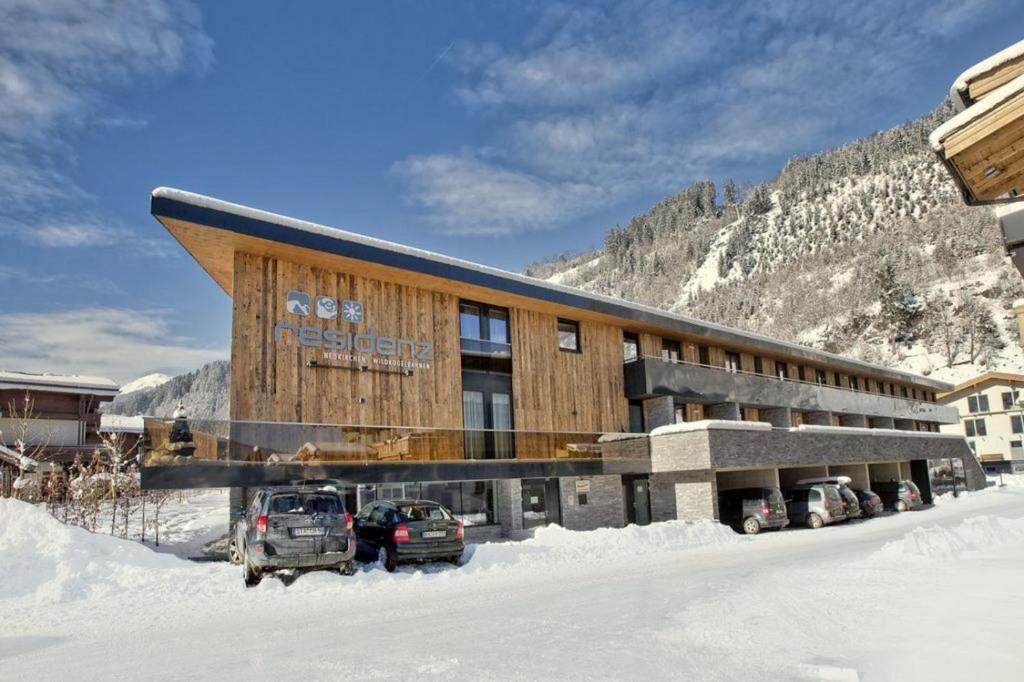 un grand bâtiment avec des voitures garées dans la neige dans l'établissement Residenz Wildkogelbahnen Top 3, à Neukirchen am Großvenediger
