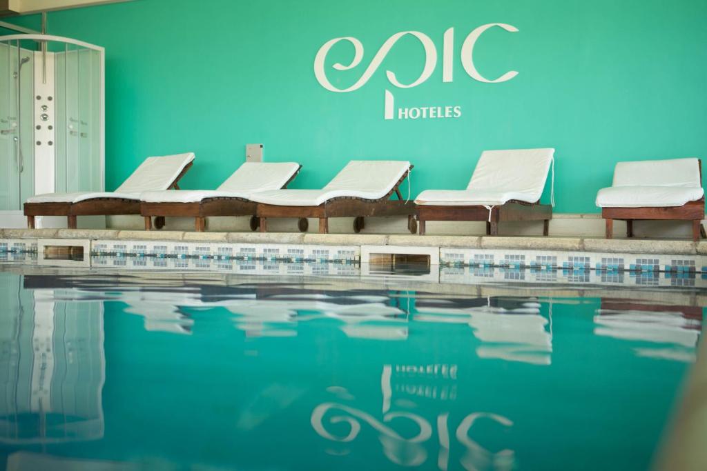 a swimming pool with white chairs and a blue wall at Epic Hotel San Luis in La Punta