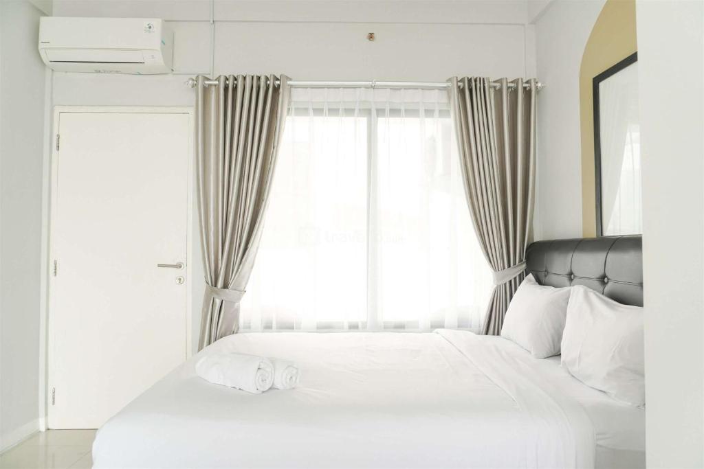 a bedroom with a white bed with a large window at Studio Loft No Kitchen Mezzanine at Kubikahomy Apartment By Travelio in Tangerang