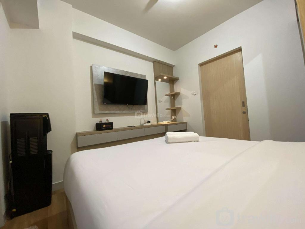 a bedroom with a white bed and a flat screen tv at Comfort and Cozy Stay 1BR at The Alton Apartment By Travelio in Semarang