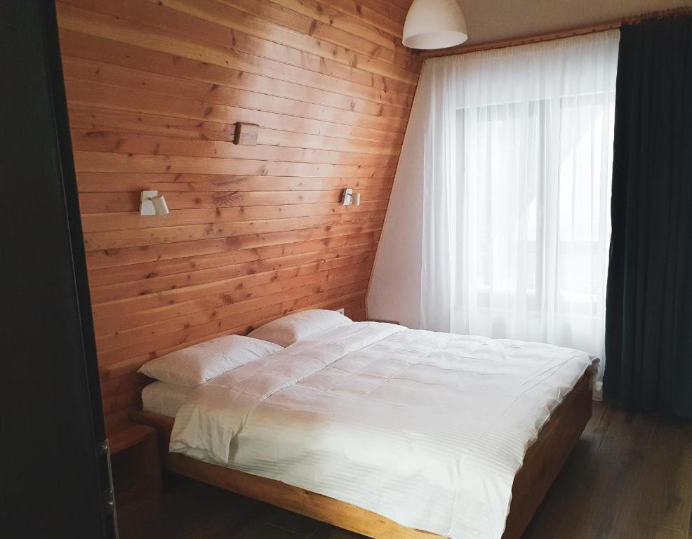 Un dormitorio con una cama blanca con una pared de madera. en Gray River Resort, en Obârşia Lotrului