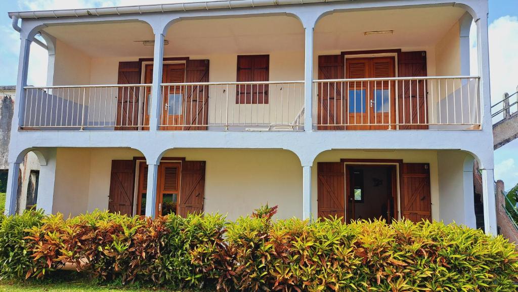 a white building with balconies and bushes at Le Pavillon des Alizés in Gourbeyre