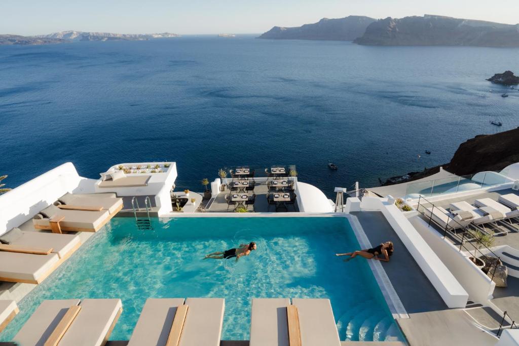 two people swimming in a swimming pool in the ocean at La Perla Villas and Suites - Adults Only in Oia