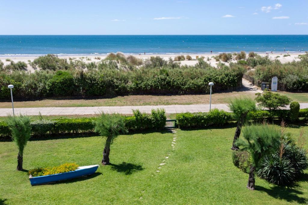 un parc avec une plage et un bateau bleu sur l'herbe dans l'établissement Chez Fabienne - Superbe appartement avec vue sur la mer et parking, à La Grande Motte