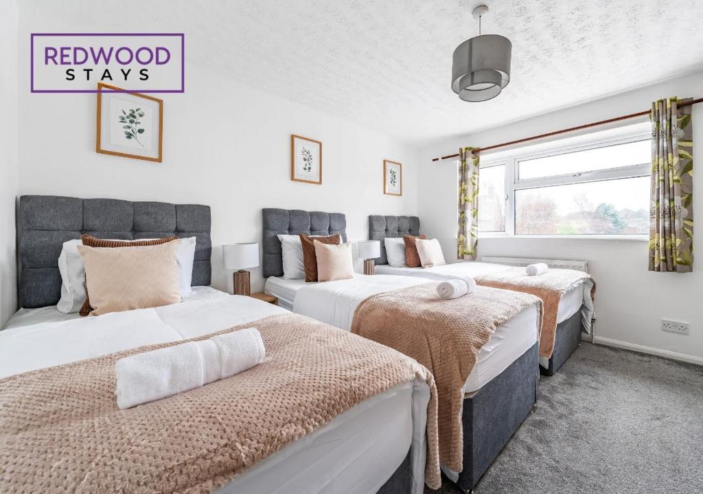 a bedroom with three beds and a window at Cosy 3-Bedroom Serviced House with Free Fast WiFi and Parking for 2 Cars By Redwood Stays in Camberley