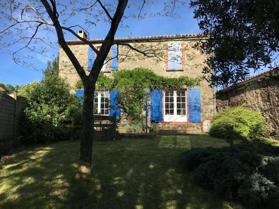 une vieille maison en briques avec des portes bleues et un arbre dans l'établissement Maison aux volets bleus, à Pouzauges