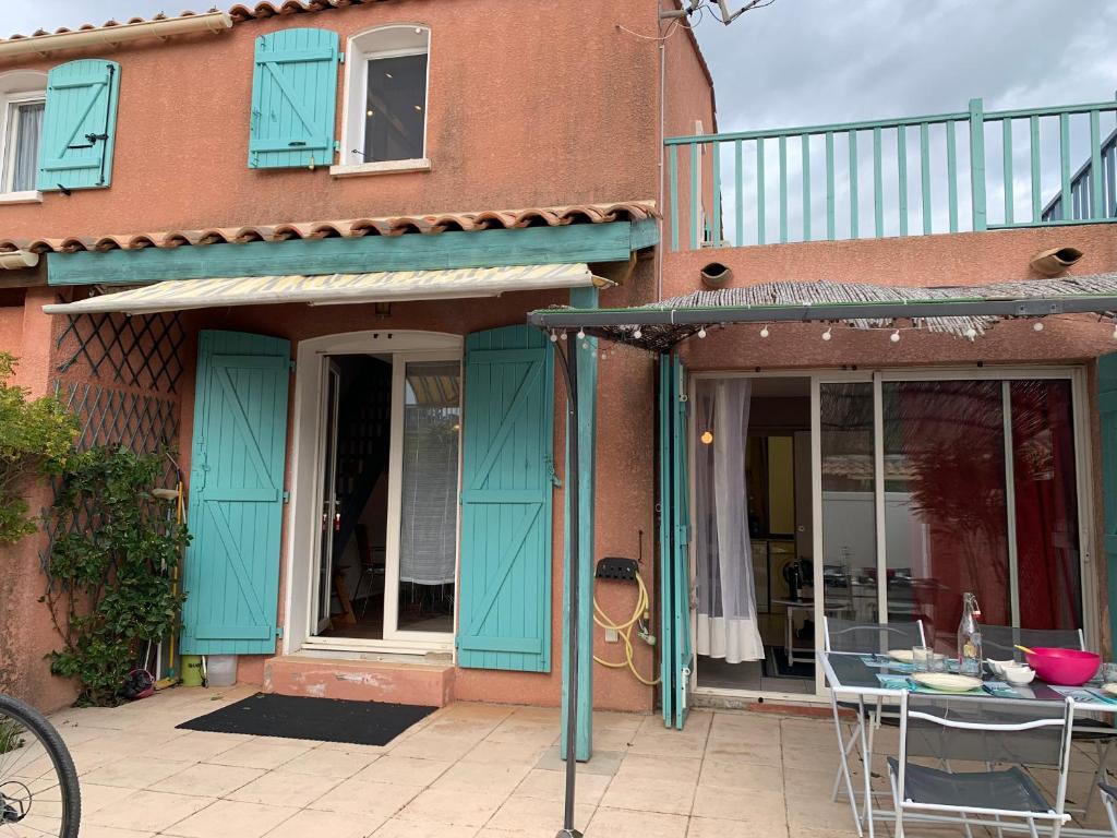 une maison avec des portes bleues et une table sur un patio dans l'établissement Villa Confortable 6 Pers. Climatisée, Proche Plage du Grazel, Calme, Tout Équipée, Stationnement Inclus - FR-1-796-71, à Gruissan