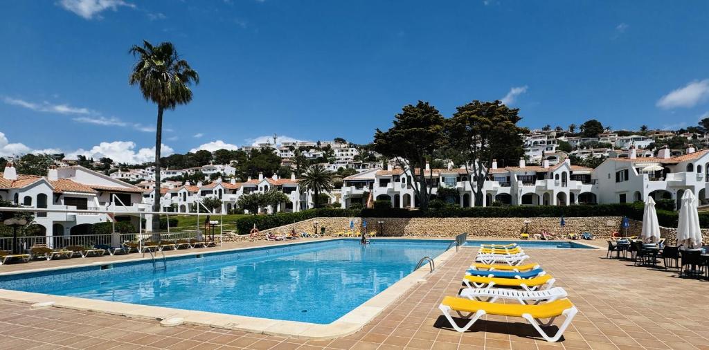 a swimming pool with yellow and white chairs and buildings at Mulberry in Son Bou