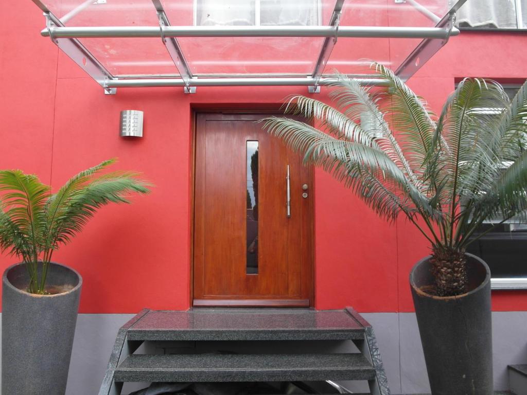 a red wall with a wooden door and two palm trees at Red Square Home in Pretoria