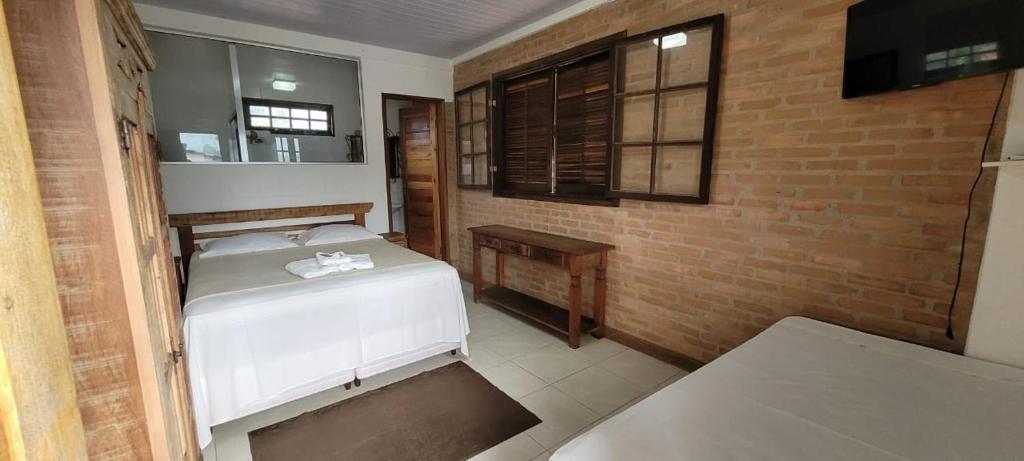 a bedroom with a white bed and a brick wall at Recanto dos Passaros centro Penedo RJ in Penedo