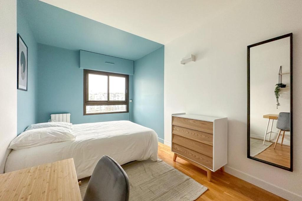 - une chambre avec des murs bleus, un lit et un miroir dans l'établissement Flexliving - room - Hillairet, à Paris