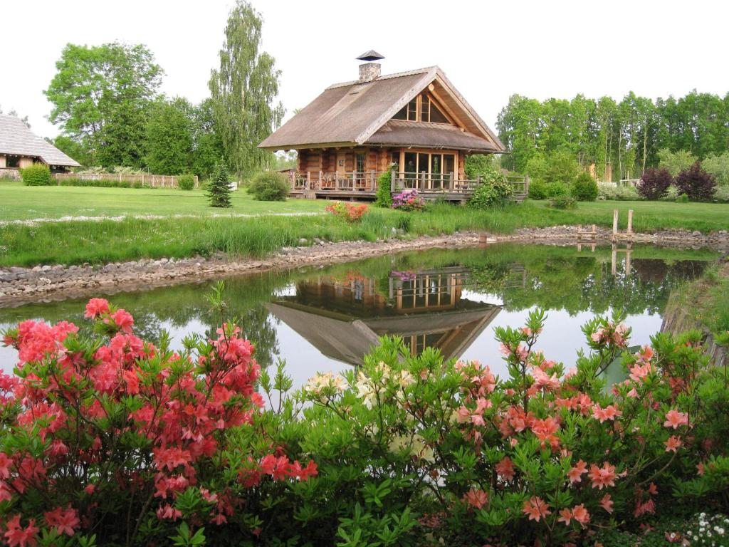 eine Blockhütte neben einem Teich mit Blumen in der Unterkunft Pilskalni in Sigulda