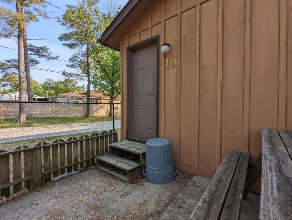 una porta di un edificio con una panchina e un cestino della spazzatura di Tiny Wood Cottage 19 a Wasaga Beach