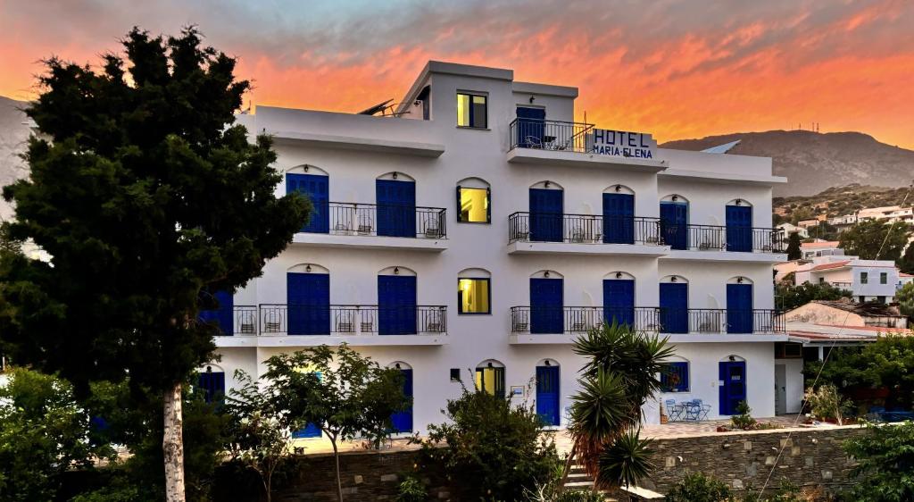 a white building with blue windows and a sunset at Hotel Maria-Elena in Agios Kirykos
