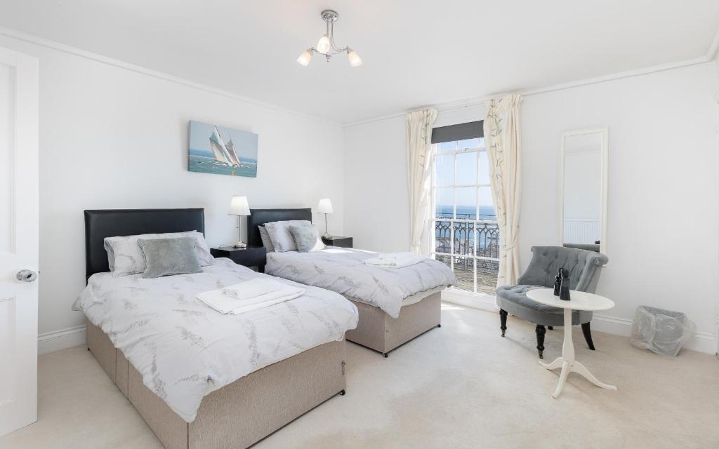 a white bedroom with two beds and a chair at Cliffhanger 18 Castle Road in Cowes