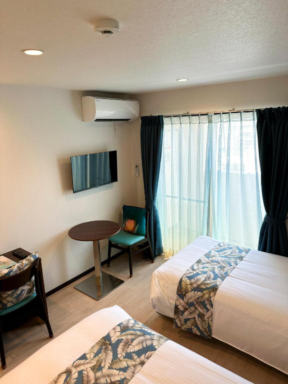 那覇市にあるKOHALA　HOTELのベッド2台、テーブル、窓が備わるホテルルームです。