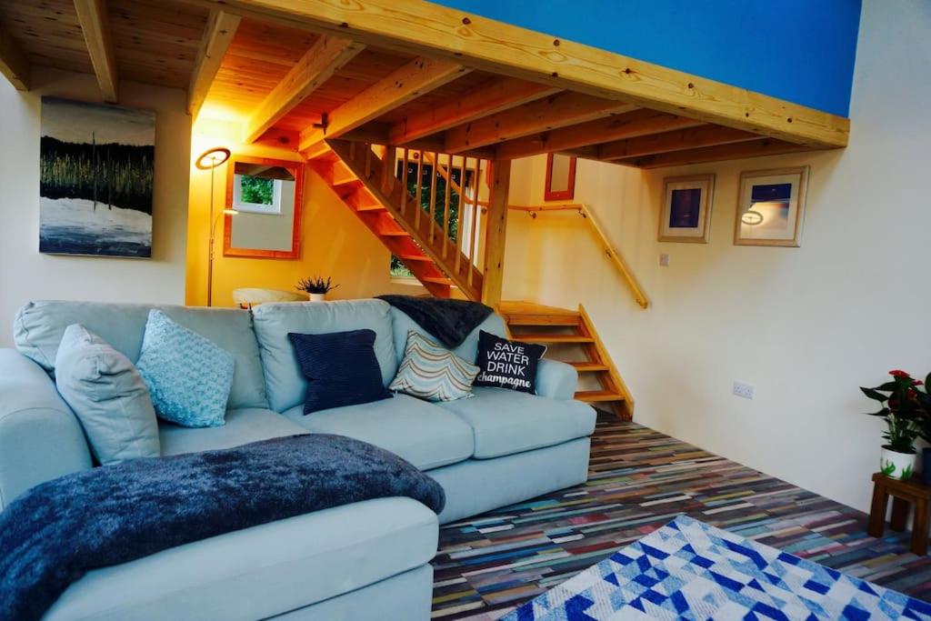 a living room with a couch and a staircase at The Hideaway, Castle an Dinas, Cornwall TR9 6JB in Saint Columb Major