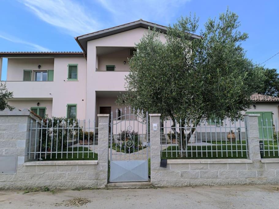 a white house with a fence and a tree at Everything a bike ride away! 10 mins to the beach with free parking! in Marina di Grosseto